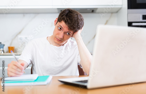 Upset man with laptop and utility bills in kitchen