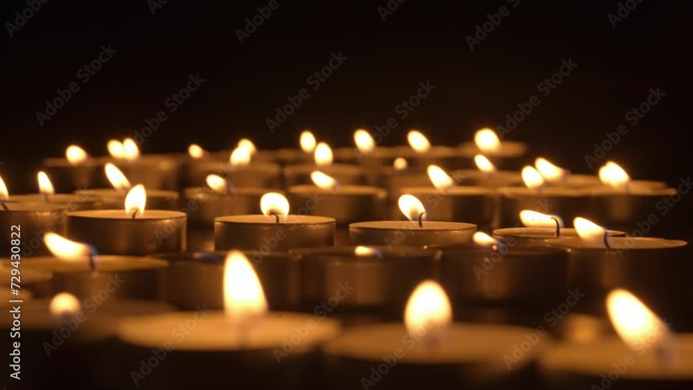 Rows of burning candles. The candles burn against a black background and the flames move when the wind blows. The concept of a memorial day. Background for advertising and design projects. Rows of burning candles. The candles burn against a black background and the flames move when the wind blows. The concept of a memorial day. Background for advertising and design projects.