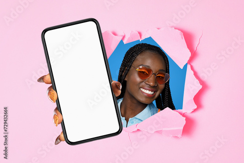 african american lady in sunglasses presenting smartphone through ripped backdrop © Prostock-studio