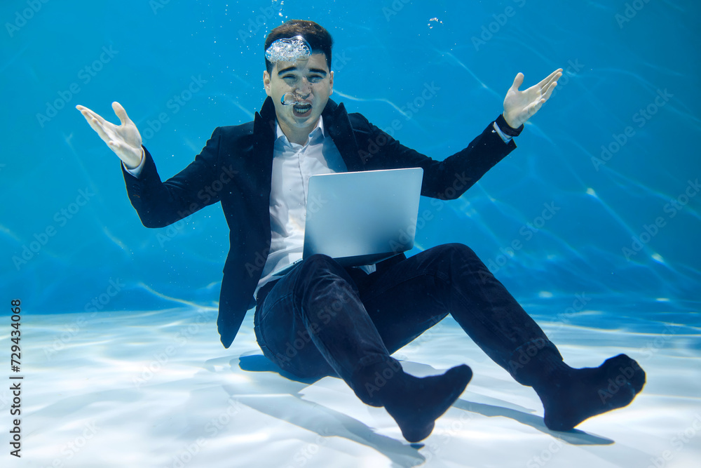 Artistic business concept. A man in a business style sits with a laptop underwater on a blue background