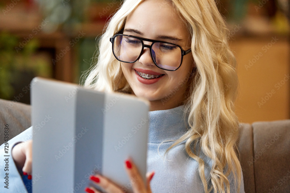 Young teen girl, student in orthodontic braces looking at tablet and make order online from home. Concept of youth and healthcare, medicine and beauty, confidence and selfcare. Young teen girl, student in orthodontic braces looking at tablet and make order online from home. Concept of youth and healthcare, medicine and beauty, confidence and selfcare.