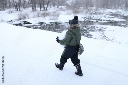 A boy carries a ball of snow across a bridge over a river
