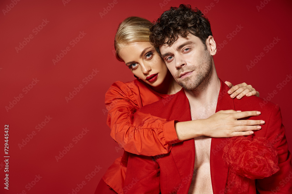 Obraz premium beautiful young woman with red lips and blonde hair embracing handsome man in red attire, fashion