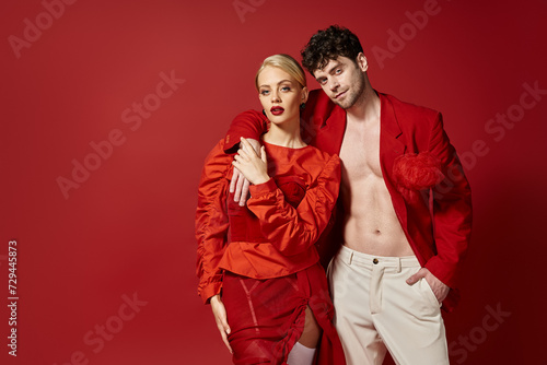 stylish man in red blazer and white pants posing while putting hand around neck of blonde woman