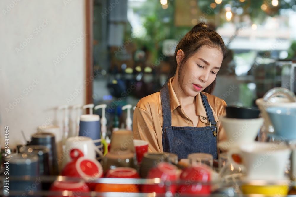 Small business woman, young Asian barista, owner of small, family-run cafe Asian pensioner mother. attentively making coffee orders customers coffee machine tilting head slightly. come cafe service