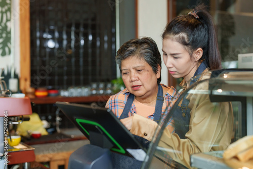 Elderly Asian shop owner retired age pensioner employee small business cafe A single business woman and her Asian daughter are checking sales at the cash register Family business minimalist style