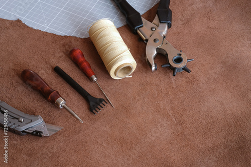 tool kit for leatherworking, thread with awl and hole puncher tools lay on suede leather hide from above view photo