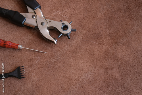 set of leather craft tools as hole punch pliers with awl on brown suede hide background