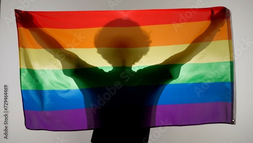 Person silhouette holding rainbow flag against white background. Silhouette of man with LGBT pride flag holding in hands. photo