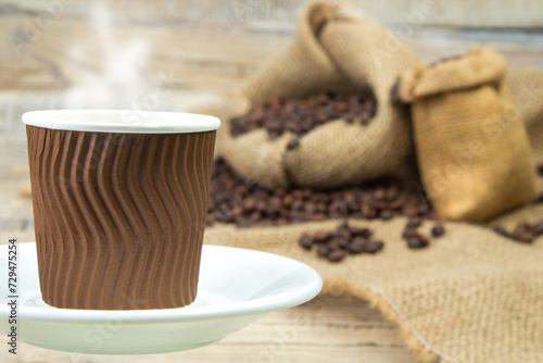 Opened burlap bags, a cup of coffee, scattered whole coffee beans on a white background.