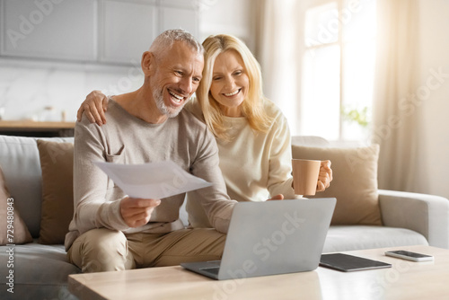Happy couple of pensioners sitting using computer at home photo
