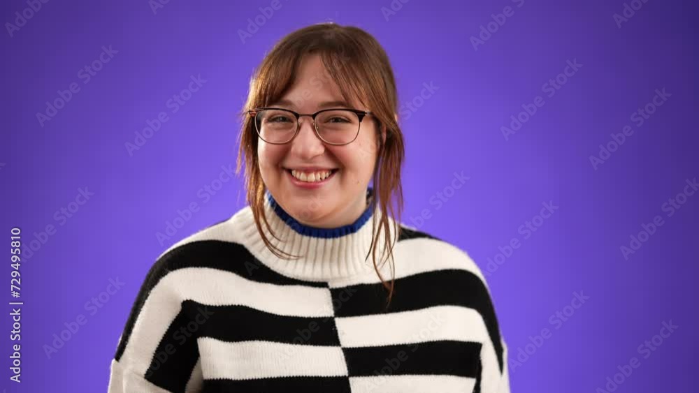 Young happy woman with brown hair wearing glasses and sweater blowing kiss as love gesture, isolated on purple background with copy space. Young happy woman with brown hair wearing glasses and sweater blowing kiss as love gesture, isolated on purple background with copy space.