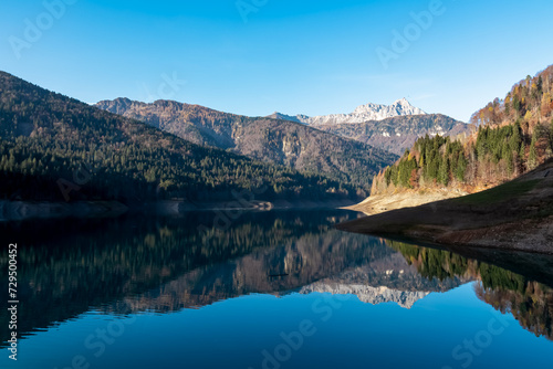 Scenic view of alpine lake Sauris (Lago di Sauris) in Friuli Venezia Giulia, Italy. Looking at water reflection of majestic mountain ridges of Carnic Alps. Serene tranquil atmosphere in Italian Alps