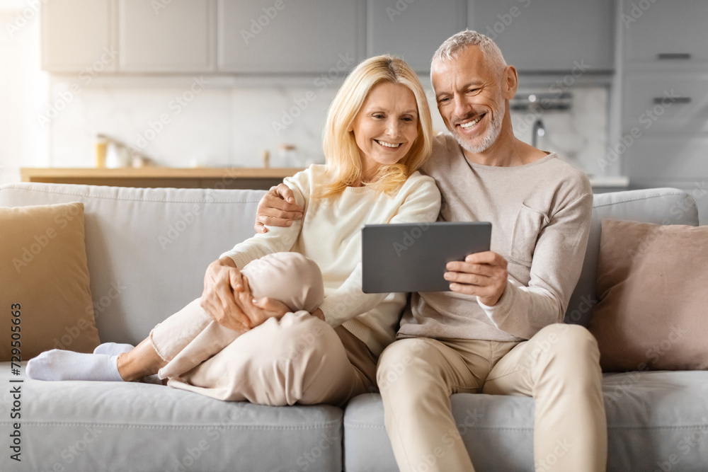 Positive beautiful loving senior spouses using digital tablet at home Positive beautiful loving senior spouses using digital tablet at home