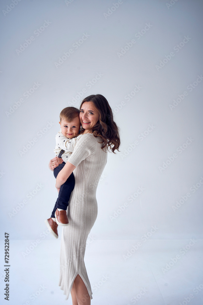 beautiful mother holds her son in her arms in a minimalistic studio beautiful mother holds her son in her arms in a minimalistic studio