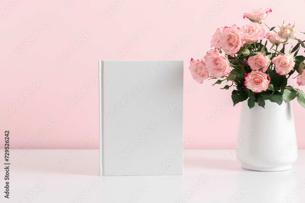 White book mockup, diary, cover, white table, pink roses on pink background. Front view. Place for text, copy space, mockup White book mockup, diary, cover, white table, pink roses on pink background. Front view. Place for text, copy space, mockup