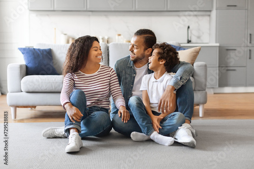 Smiling black family of three sitting on floor in living room