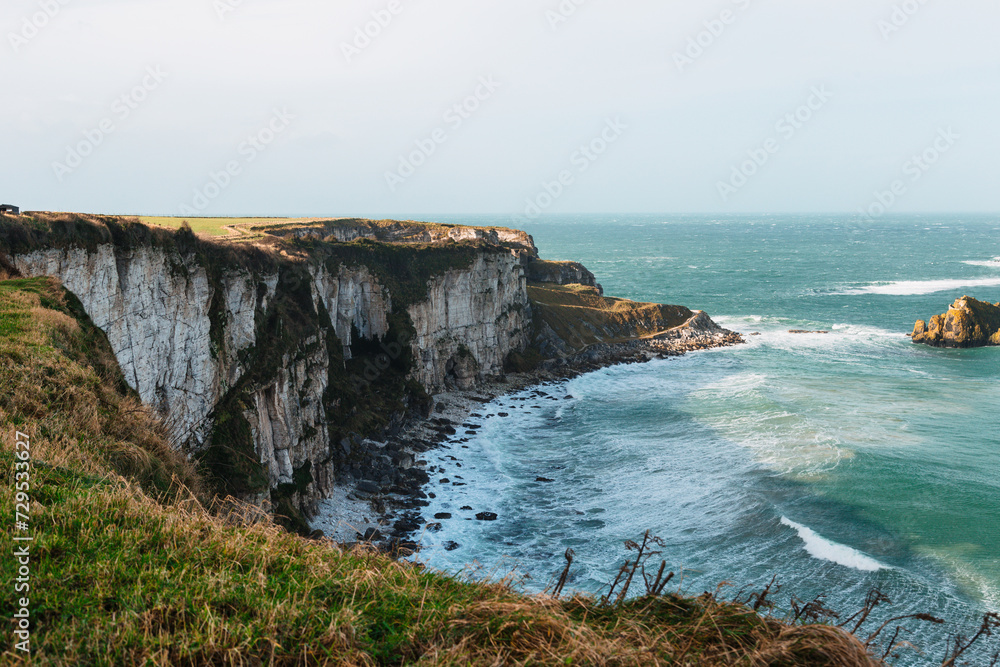 A stunning backdrop of cliffs on a cloudy day in Northern Ireland, where the vibrant blue waves crash against the rocky shore