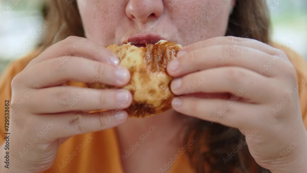 Unrecognizable woman brings greasy fast food dish to her mouth and bites it. High calorie food in crowded summer cafe. Close up push in shot of chewing mouth with fat lips of lady with big cheeks. Unrecognizable woman brings greasy fast food dish to her mouth and bites it. High calorie food in crowded summer cafe. Close up push in shot of chewing mouth with fat lips of lady with big cheeks.