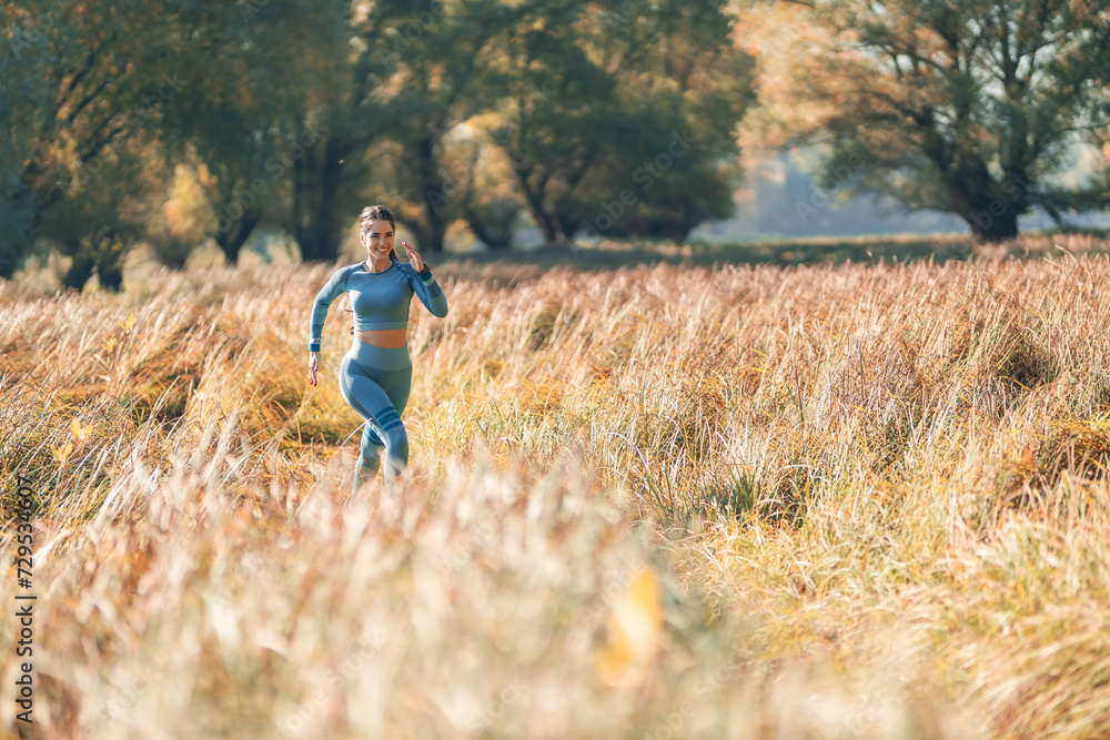 A distant shot of a happy athletic young woman running in a rural area on a sunny morning