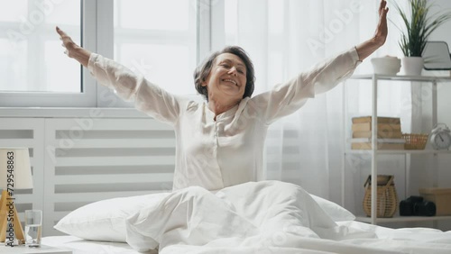 Joyful senior wakes up, stretches in bed, embracing morning, symbol of vitality photo