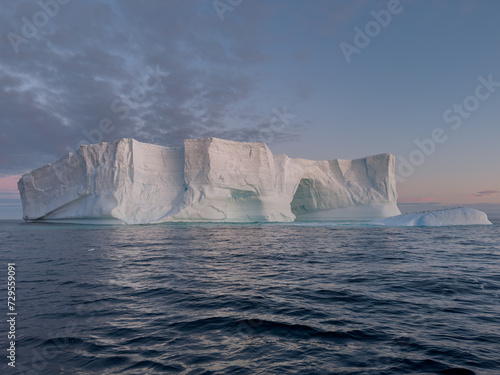 A huge high breakaway glacier drifts in the southern ocean off the coast of Antarctica at sunset  the Antarctic Peninsula  the Southern Arctic Circle  azure water  cloudy weather