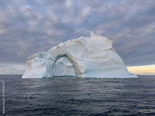 A huge high breakaway glacier drifts in the southern ocean off the coast of Antarctica at sunset, the Antarctic Peninsula, the Southern Arctic Circle, azure water, cloudy weather