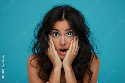 Nervous Latin woman in studio with oops reaction to gossip on blue background. Mistake, sorry and female overwhelmed by fake news