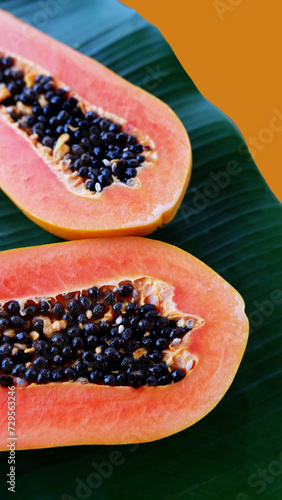 Ripe papaya placed on a banana leaf. Slice papaya with a banana leaf isolated on an orange background. The concept of fresh fruit, healthy eating, and organic food. Close-up papaya seeds texture.