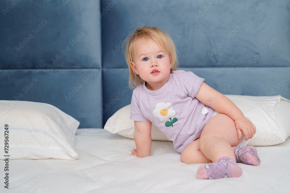 Little child blonde is smiling lying on the bed linen Little child blonde is smiling lying on the bed linen