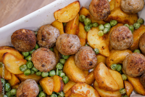 Delicious hot lunch from the oven potato slices, meatballs and green peas