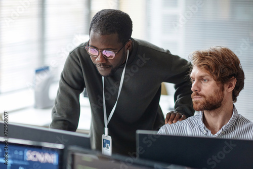 Portrait of young Black man mentoring bearded IT developer and reviewing code looking at computer screen in office