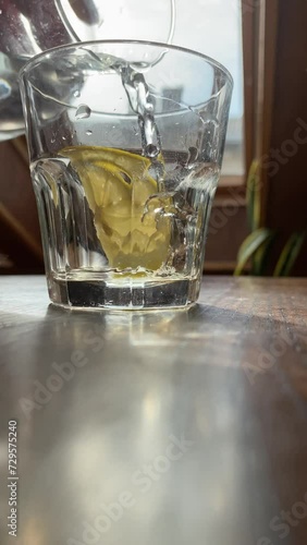 Vertical screen: Close up glass of water, soft focus. Pouring purified fresh clean drink water into glass from the bottle on old wooden table in sunlight nature background. Feel refreshing morning.