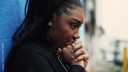 One pensive young black woman pondering decision with hands clenched together standing outside with thoughtful gaze struggling with dilemma in in urban setting photo