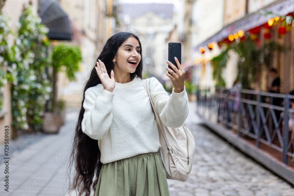 Fototapeta premium Joyful indian woman using smartphone for video call on city street