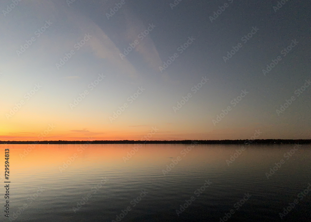 Distant shore highlighted by vibrant sunset colors reflected in still water
