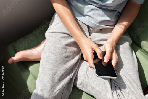 Person sitting and holding mobile phone in hands, scrolling websites or social media, or messaging online by internet at home, natural sun light, soft selective focus, lifestyle