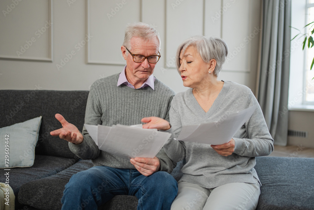 Sad tired disappointed middle aged senior couple sit with paper document. Unhappy older mature man woman reading paper bill managing bank finances calculating taxes planning loan debt pension payment Sad tired disappointed middle aged senior couple sit with paper document. Unhappy older mature man woman reading paper bill managing bank finances calculating taxes planning loan debt pension payment