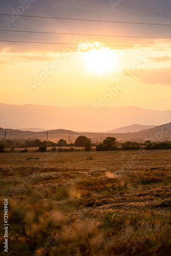 Stunning sunset over the countryside of Bulgaria. Mountain hills in the distance. Beautiful yellow orange skies and trees in the distance.