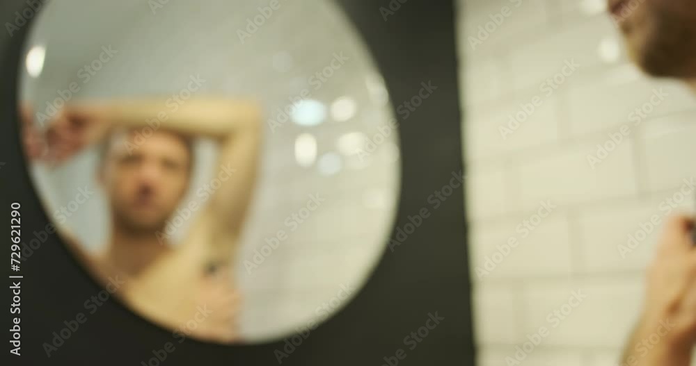 Blurred young man shaves his armpits with an electric trimmer, reflection in the bathroom mirror Blurred young man shaves his armpits with an electric trimmer, reflection in the bathroom mirror