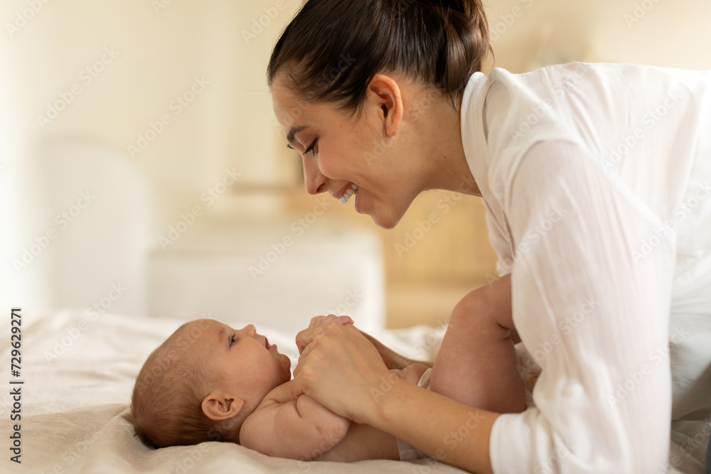 Caring young mother playing with her newborn baby daughter in the bed and looking at her with smile, happy moments of maternity Caring young mother playing with her newborn baby daughter in the bed and looking at her with smile, happy moments of maternity