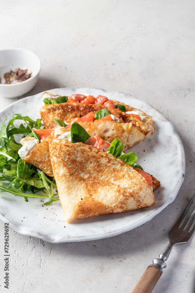 Crepes or thin pancakes with smoked salmon, soft cheese and spinach on a plate on gray textured background. Pancake day, Maslenitsa, text space Crepes or thin pancakes with smoked salmon, soft cheese and spinach on a plate on gray textured background. Pancake day, Maslenitsa, text space