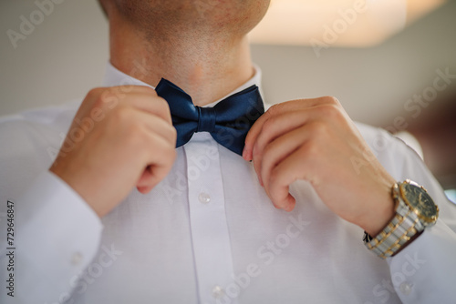 Valmiera, Latvia - July 7, 2023 - Close-up of a man adjusting a blue bow tie and wearing a wristwatch.