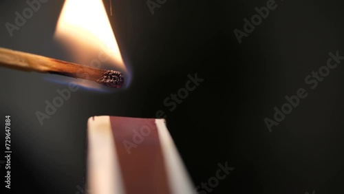 Strikes a match on the side of the box. Smoke and fire appear. The flame ignites. Match lights up. Hands lights a match with a green sulfur head. burns. Super macro shot. Extreme close-up photo