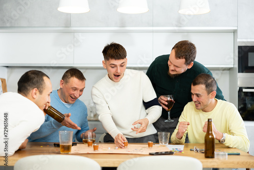 Group of adult friends excitedly playing board games and drinking beer at home