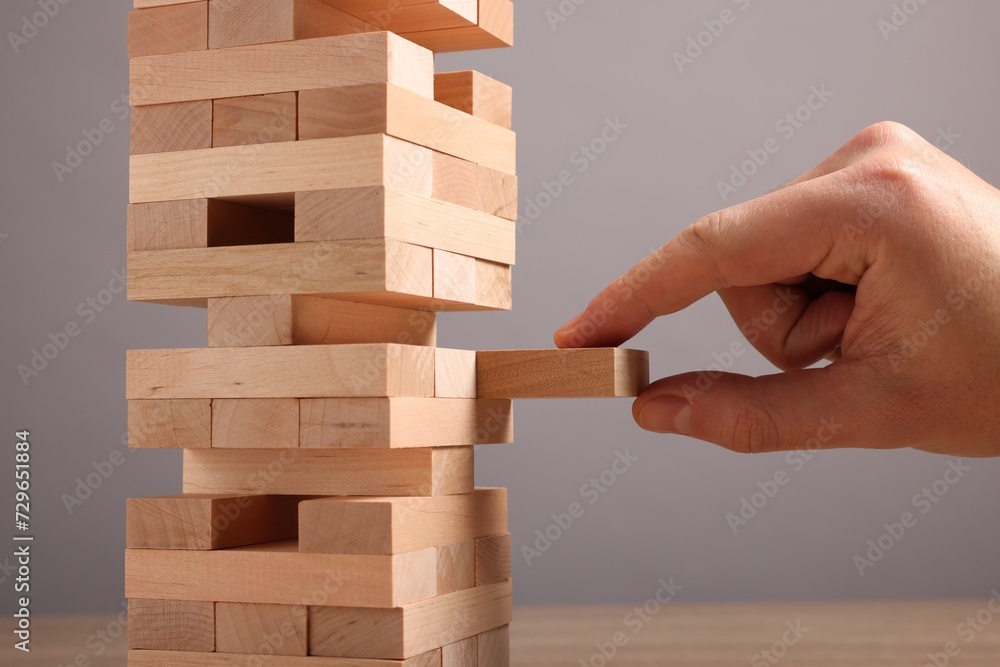 Playing Jenga. Man removing wooden block from tower at table against grey background, closeup Playing Jenga. Man removing wooden block from tower at table against grey background, closeup