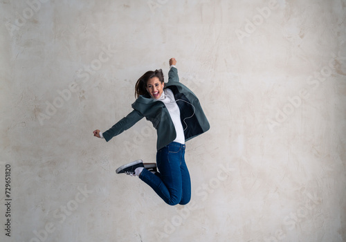 Freedom, success and jump, young woman with energy and motivation in celebration of winner deal. Ecstatic female with in-ear headphones, jump for joy.