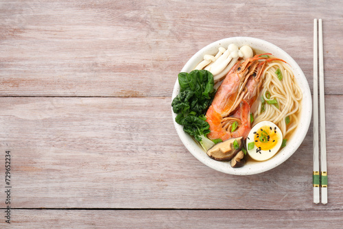 Delicious ramen with shrimps and egg in bowl and chopsticks on wooden table, top view with space for text. Noodle soup