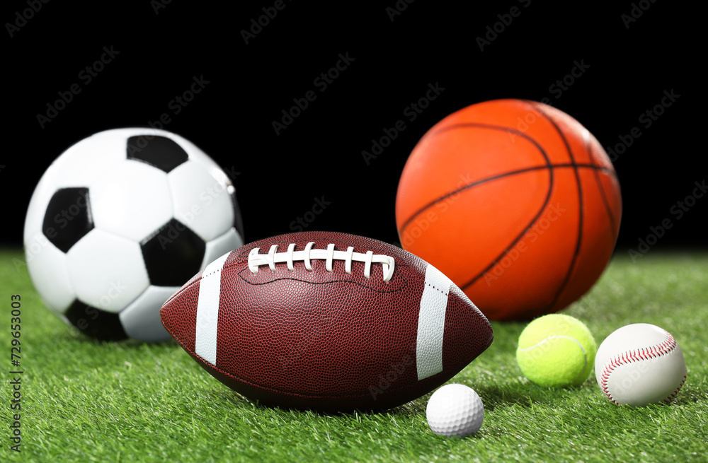 Many different sports balls on green grass against black background