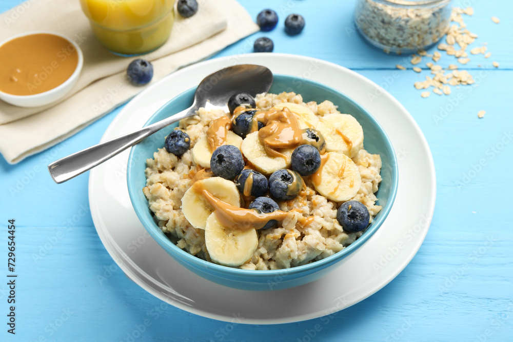 Tasty oatmeal with banana, blueberries and peanut butter served in bowl on light blue wooden table Tasty oatmeal with banana, blueberries and peanut butter served in bowl on light blue wooden table